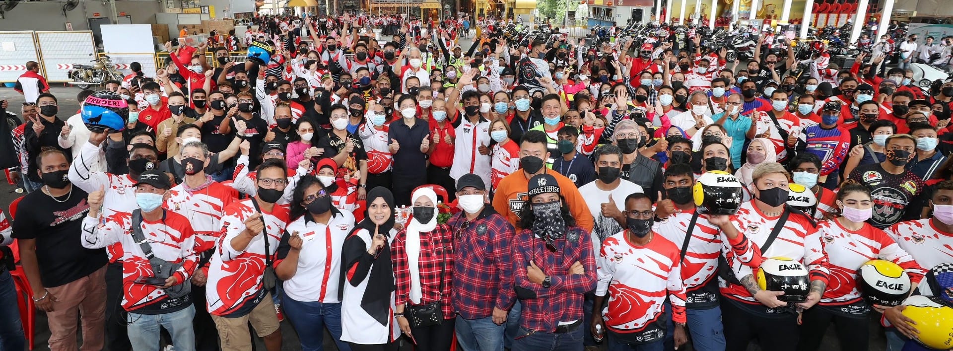 Large group of people wearing masks and red/white shirts, some holding motorcycle helmets.